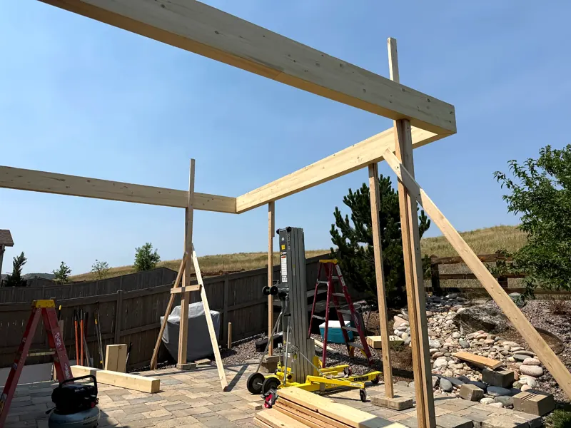 Timber pergola frame under construction above a paved patio