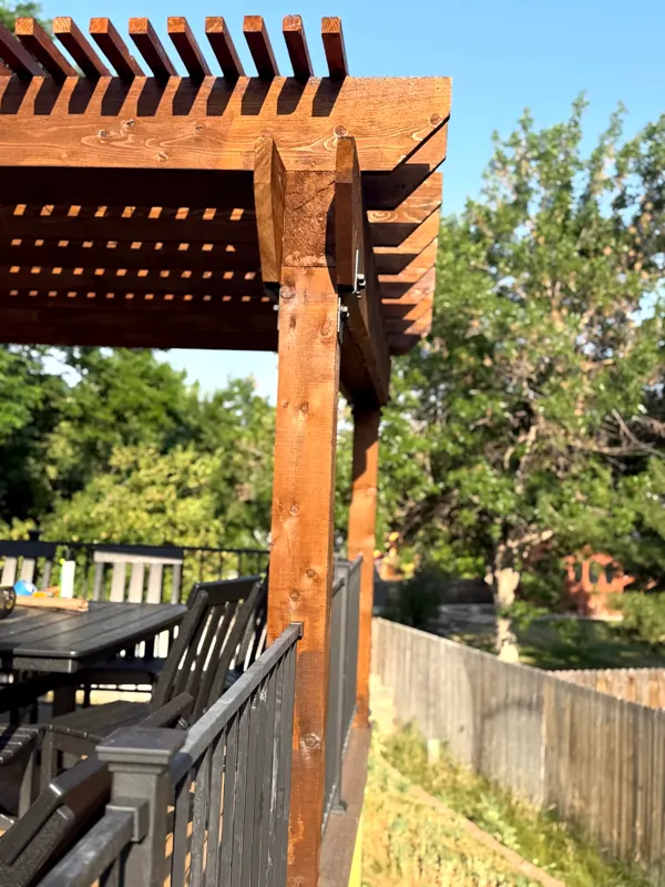Corner of a timber pergola with black deck railings and trees behind