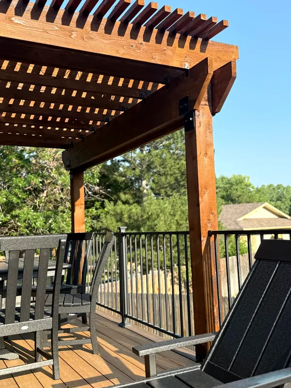 View from beneath a stained timber pergola over a deck with dining chairs